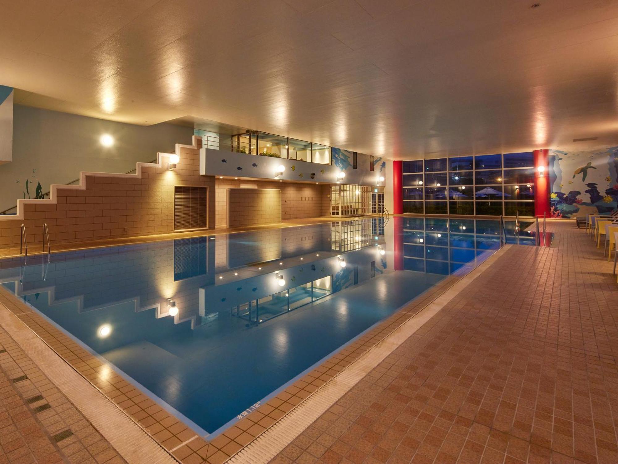 מלון Urayasu Grand Nikko Tokyo Bay Maihama מראה חיצוני תמונה The photo shows an indoor swimming pool area. The pool features a calm blue water surface and is surrounded by tiled flooring. There is a staircase leading to a higher level, likely providing access to a lounge or seating area. Large windows allow na